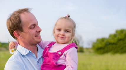 Fototapeta premium Male European race holding a little girl European race. Background is a green meadow. Happy dad and daughter. International Children Day. 
