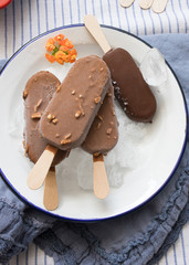 Four chocolate ice creams on a dish full of ice cubes. Three on a pile and the black one isolated.