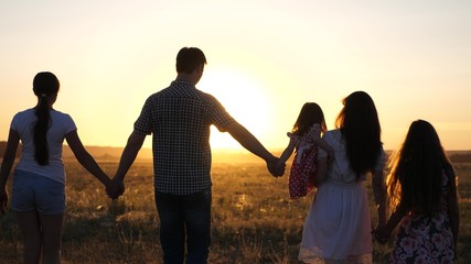 free Happy family walks in field in sunset light. healthy dad mom and daughters walk in park in sunshine. children and parents travel on vacation. happy father carries a child. happy childhood concept