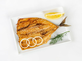 fried mackerel lying on a rectangular plate with onion rings and a slice of lemon top view on a white background