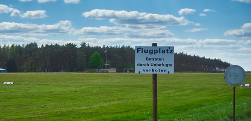 Empty airfield for gliders on a grassy area with a sign with German inscription: airfield, no trespassing