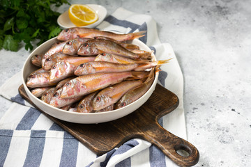 Black sea barabulka fish in a white ceramic bowl on a light gray kitchen table. A lot of fish red mullet. Black sea barabulka