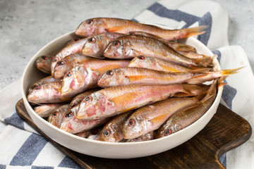 Black sea barabulka fish in a white ceramic bowl on a light gray kitchen table. A lot of fish red mullet. Black sea barabulka