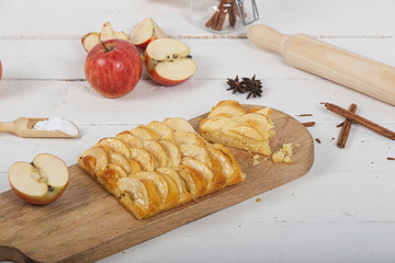 Portion of apple pie on wooden cutting board with various ingredients. Cinnamon sticks and luster...