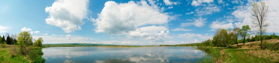 Panoramic landscape from the lake shore with colorful clouds in the spring sun.