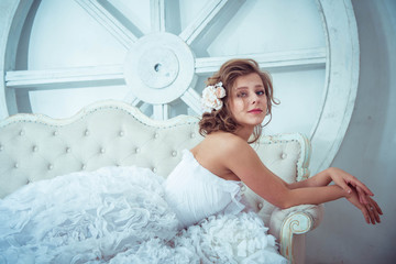 Lovely young girl bride lies on a sofa in a bright studio. wedding photo shoot. Wedding hairstyle....