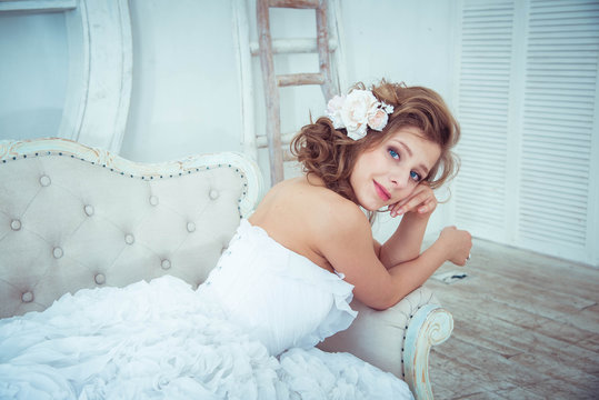 Lovely young girl bride lies on a sofa in a bright studio. wedding photo shoot. Wedding hairstyle. Fashion photography in a chic white long puffy dress