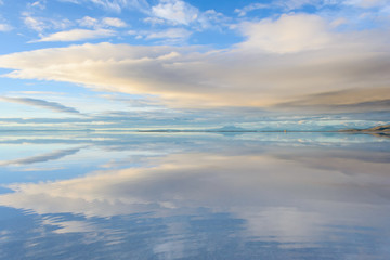 Fototapeta na wymiar Misty landscape with clouds and reflection in the lake , early morning, calm and quiet, pastel blue and golden color, Salar de Uyuni, Bolivia