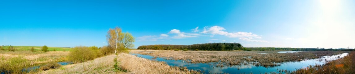 Panoramic landscape from the lake shore with colorful clouds in the spring sun.