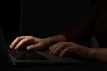 Hacker working with laptop in darkness, closeup of hands. Cyber crime