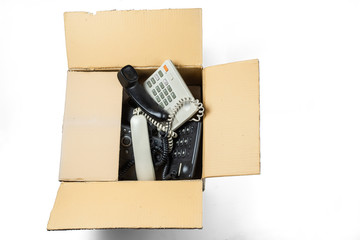 Old desk phones in a cardboard box isolated on a white background.