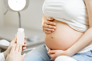 Doctor holding some medicine or supplements for a pregnant woman during a consultation, close-up view focused on pregnant belly. Concept of medication for pregnant women