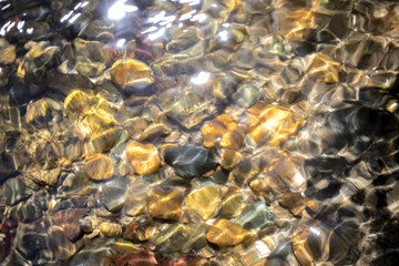 Close up of colorful stones and pebbles under water in the river. Background and texture of shiny pebbles on the river bottom at tropical forest.