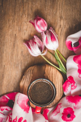 Coffee in a red mug on a wooden background, near tulips; composition of spring objects, vacation dreams
