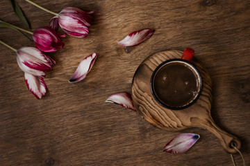 Obraz na płótnie Canvas Coffee in a red mug on a wooden background, near tulips; composition of spring objects, vacation dreams