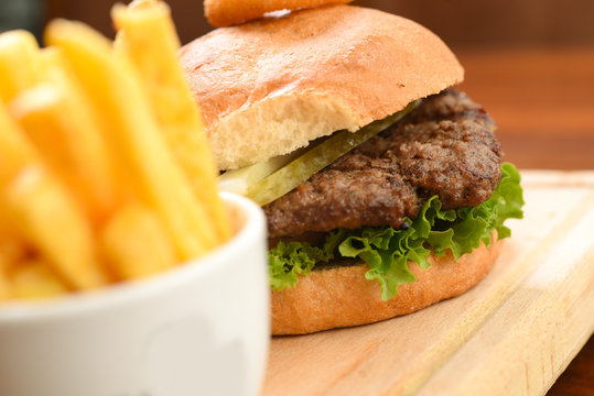 Homemade hamburger with beef, tomato, lettuce and sweet and sour sauce. French fries, onion rings. Serve on a wooden kitchen board. background image, copy space