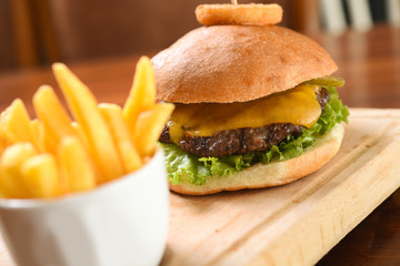 Homemade hamburger with beef, cheddar, tomato, lettuce and sweet and sour sauce. French fries, onion rings. Serve on a wooden kitchen board. background image, copy space