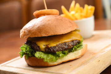 Homemade hamburger with beef, cheddar, tomato, lettuce and sweet and sour sauce. French fries, onion rings. Serve on a wooden kitchen board. background image, copy space
