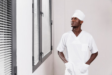 Specialist male doctor looking through the windows. Black health professional, afro american doctor, african nurse.