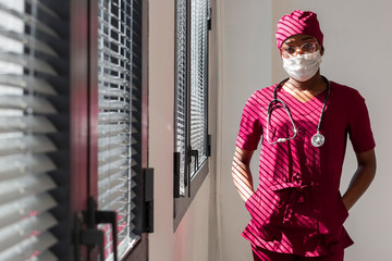 Female doctor standing next to hospital windows. Black health professional, afro american doctor, african nurse.