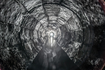 Round drainage concrete tunnel with water built with formwork. With a lantern light at the end....