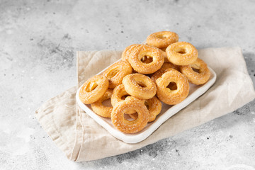 Puff pastry sprinkled with sugar in a white plate on a light gray background. Cookies sprinkled with sugar. Sweet pastries