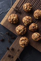 Fototapeta premium Healthy food concept. Rustic style oatmeal bites and dry alder tree branch with cones on oak board on black background top view