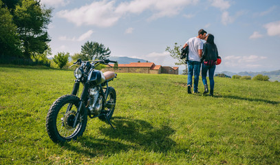 Unrecognizable couple kissing while walking on the field with parked motorbike