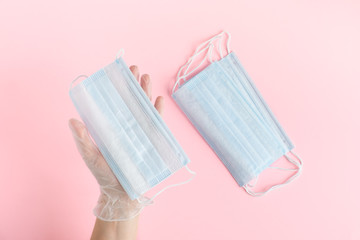 top view hand in a protective glove holds a medical face mask against viruses and bacteria on pink background, protective medical tool