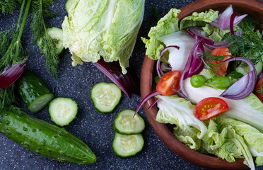 Sliced vegetable salad of cucumber tomatoes and cabbage, onions on a dark background.
