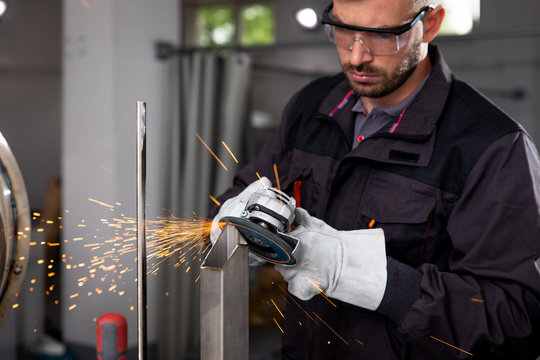 Industrial worker with angle grinder working on metal structure at workshop.