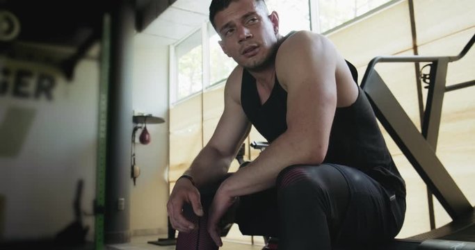 Portrait of professional muscular athletic man bodybuilder in shorts is sitting on bench in closed gym