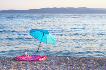 Blue beach umbrella on summer coast. Sea beach with sun umbrella is waiting for tourists on Sunset. Happy summer vacations concept.