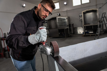 Industrial worker with angle grinder working and polishing stainless steel structure at workshop.