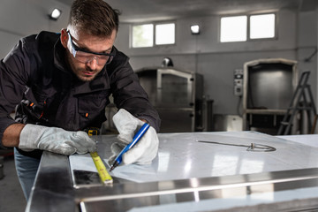 Industrial worker working on metal structure making marks with measuring meter at workshop.