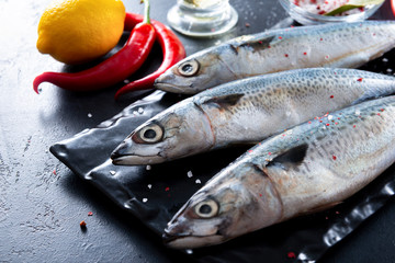 raw fish mackerel, chili pepper, lemon,  spices  on a black background close-up top view,