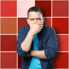 Obraz premium Young man wearing a blue outfit. Looking seriuos and covering his mouth with his hand.