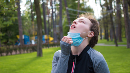 Sport during quarantine, coronavirus. Tired young athletic woman runner taking off medical protective mask and free breathing deep. Fitness woman taking a rest after running workout hard outdoors