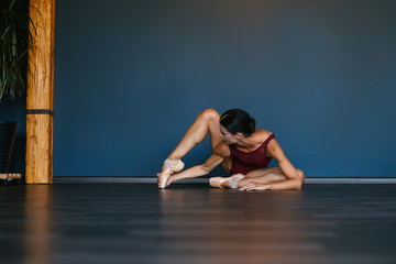 Fototapeta na wymiar Modern ballet dancer performing ballet exercise on dark studio background. Dancer in a burgundy dark red leotard