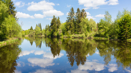 Panorama of Deixlfurter See. Bavarian landscape with lake, forest and blue, cloudy sky.