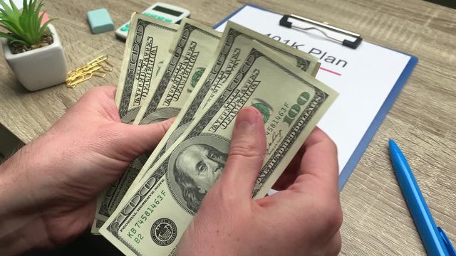 401k retirement plan, a man counts 100 dollar bills at a wooden table