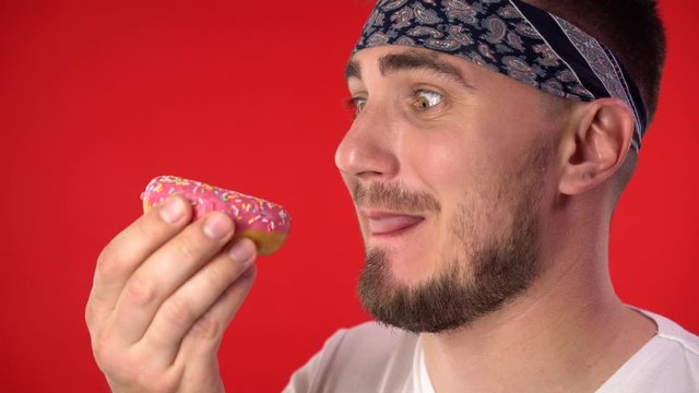 Close-up of a man with dark hair. A man holds a glazed donut in his hands, and then happily bites and eats a donut. Sweet tooth man, addiction to sweets.