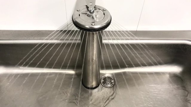 Industrial hand washing station with running water. Water running in a commercial handwashing metal sink.