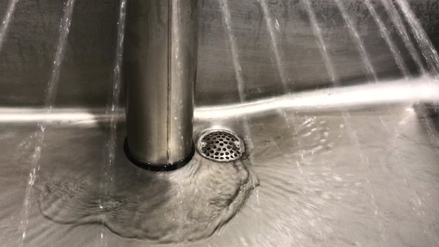A commercial sanitary washing sink with running water pouring in the drain. Industrial hand washing station with running water.