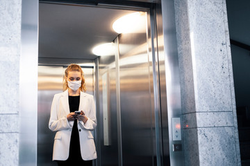 Business woman wearing protective white face mask is using elevator © seligaa