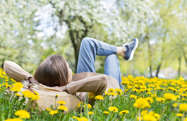 Relaxing woman lying on spring blooming meadow. Girl resting in summer park. Enjoy life, having fun, leisure, relaxation, lifestyle concept