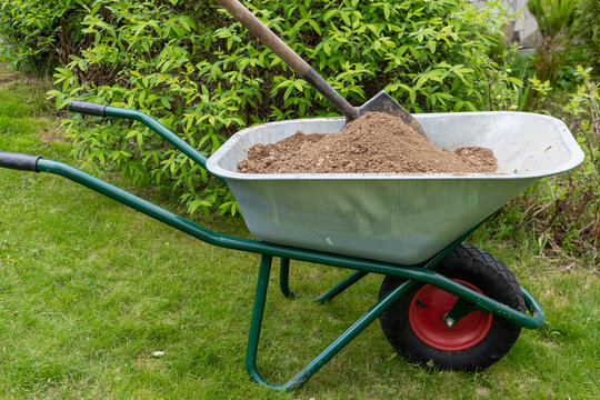 Old wheelbarrow on green grass with soil and a shovel. Side view