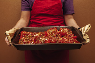 The hands of a female chef hold a baking tray with baked vegetables and meat