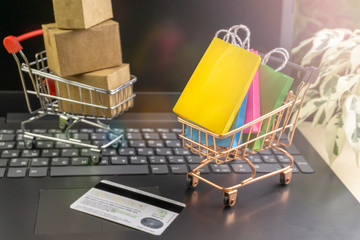 online shopping concept. little shopping cart with colorful shopping bags inside  stand near laptop, little deliver boxes, bank card
