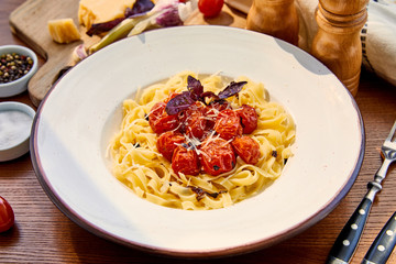 delicious pasta with tomatoes, basil and parmesan served in round plate on wooden table in sunlight